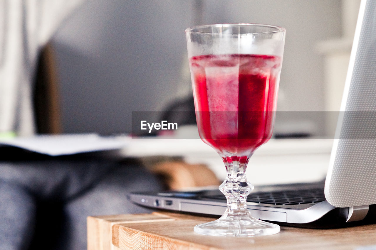 Close-up of red drink in glass by laptop on table 