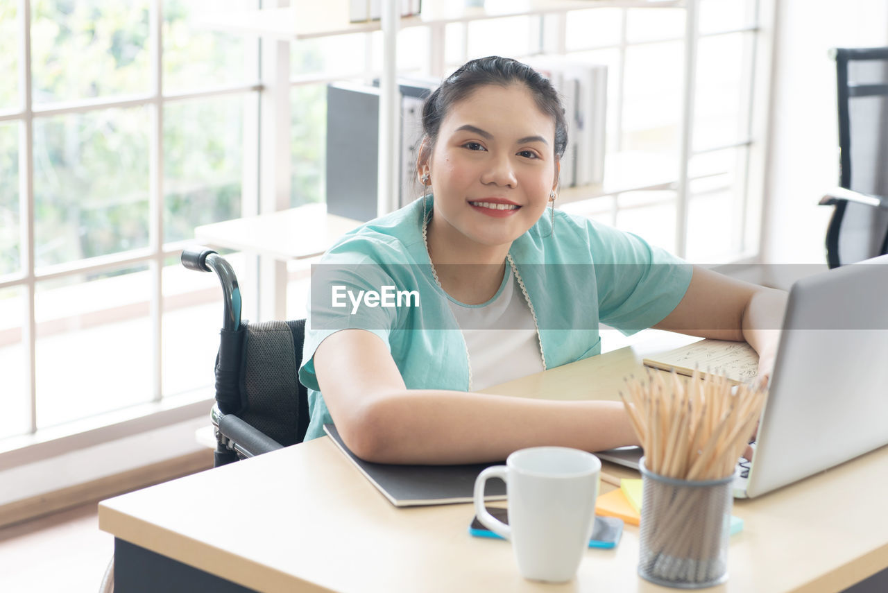 Young disabled woman sit on wheelchair using computer laptop for work at office workplace