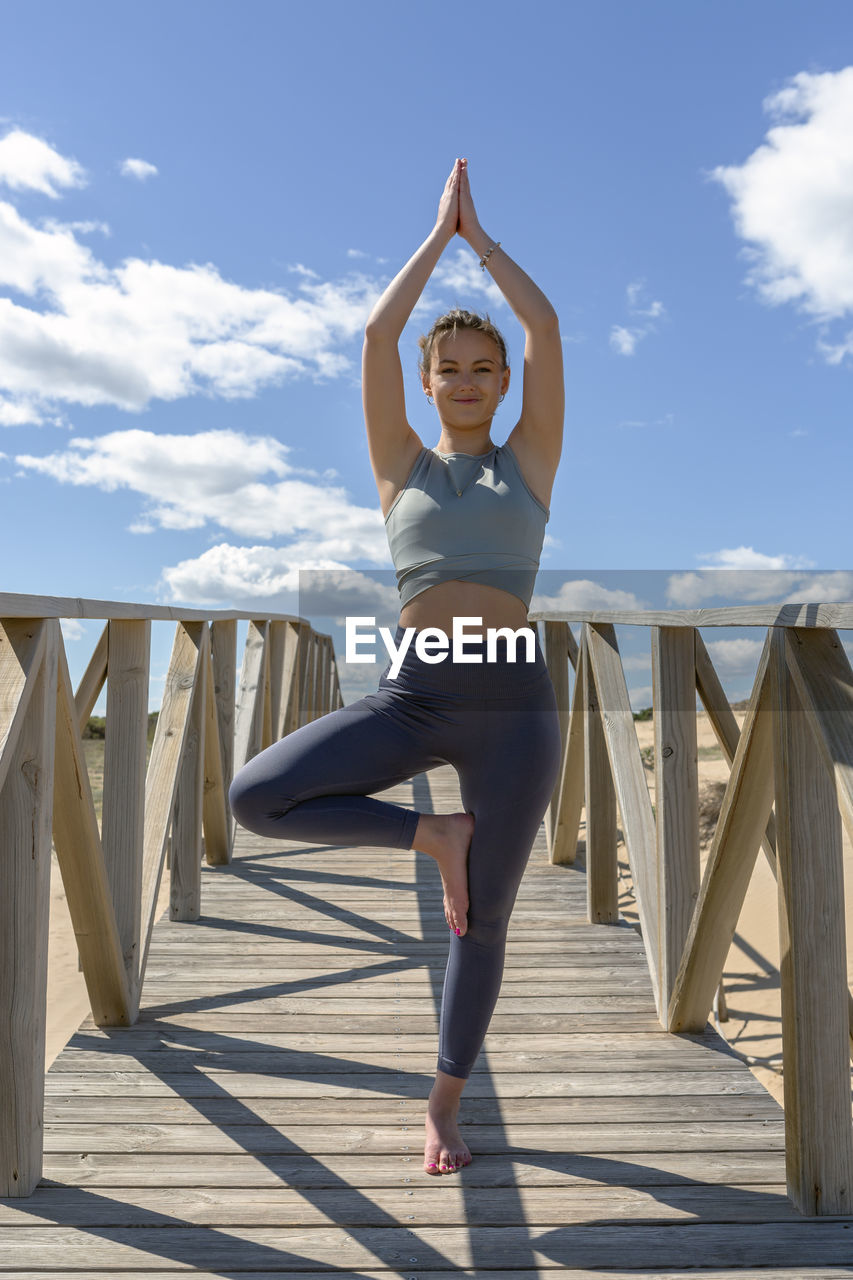 Woman performing pilates-yoga on wooden walkway next to the beach