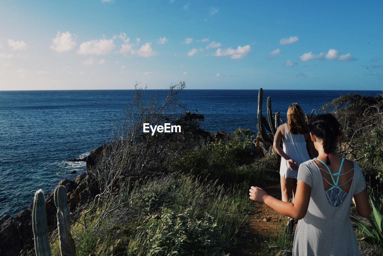 Rear view of women walking amidst plants against sea and sky