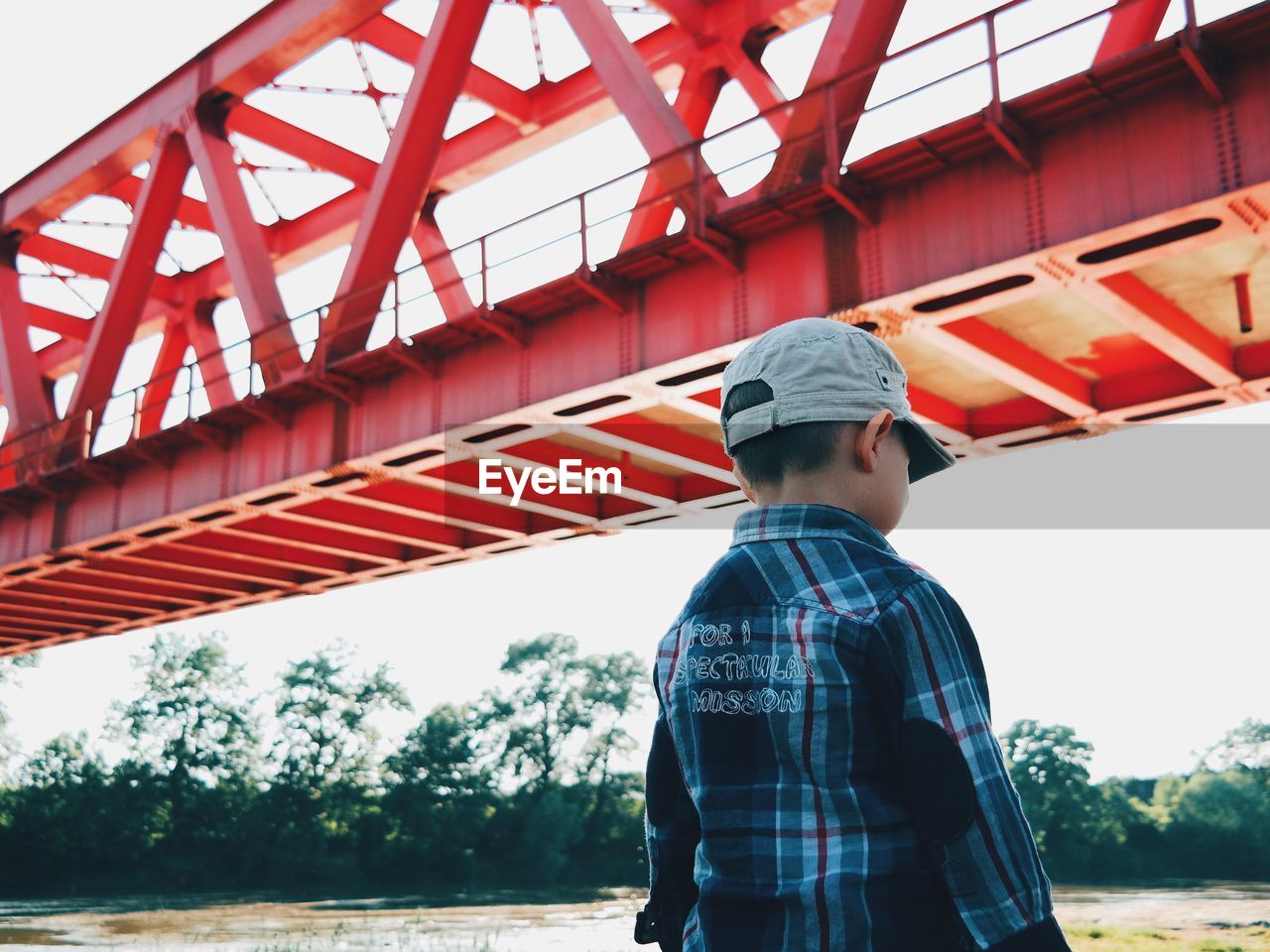 Rear view of boy standing by bridge against sky