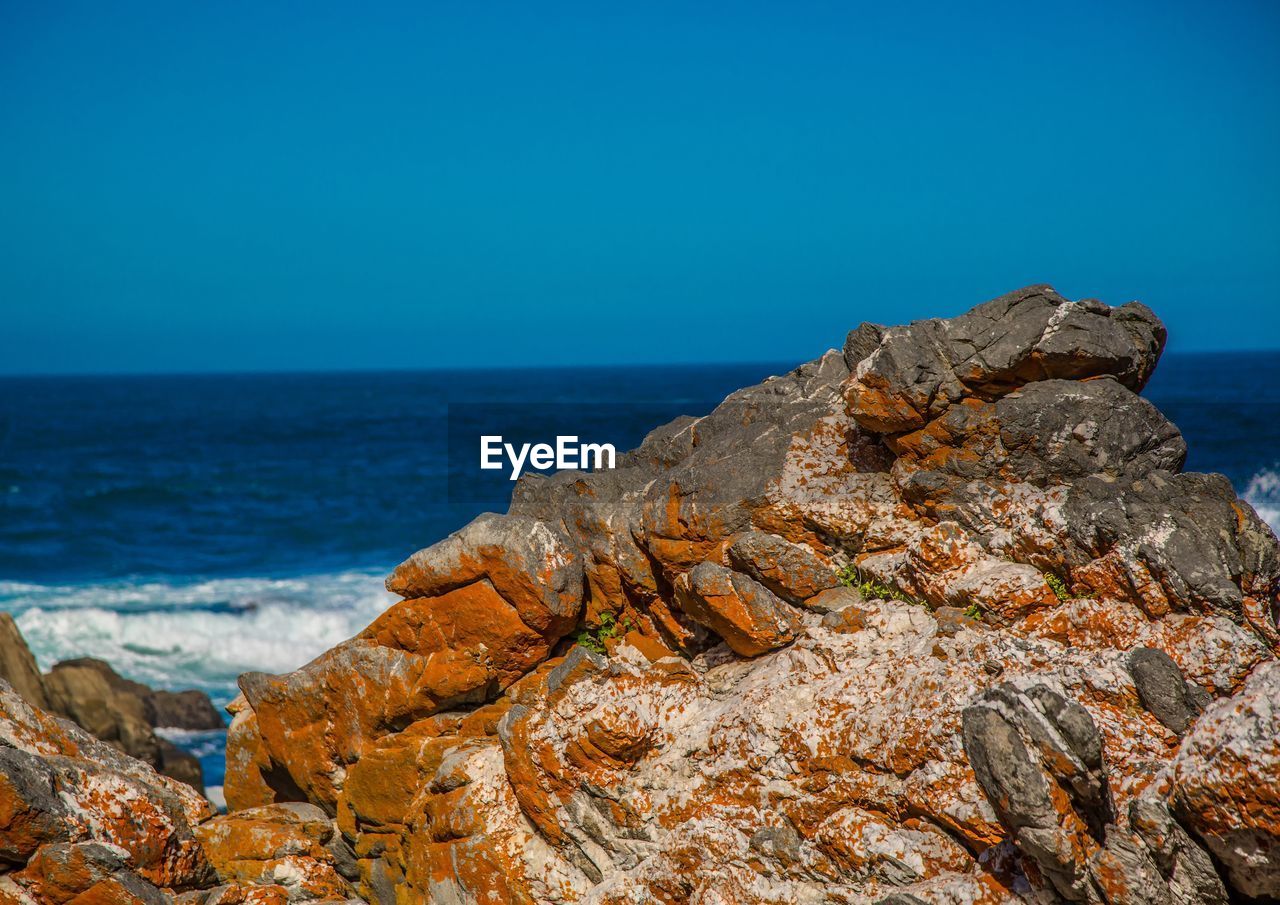 ROCK FORMATION BY SEA AGAINST CLEAR BLUE SKY