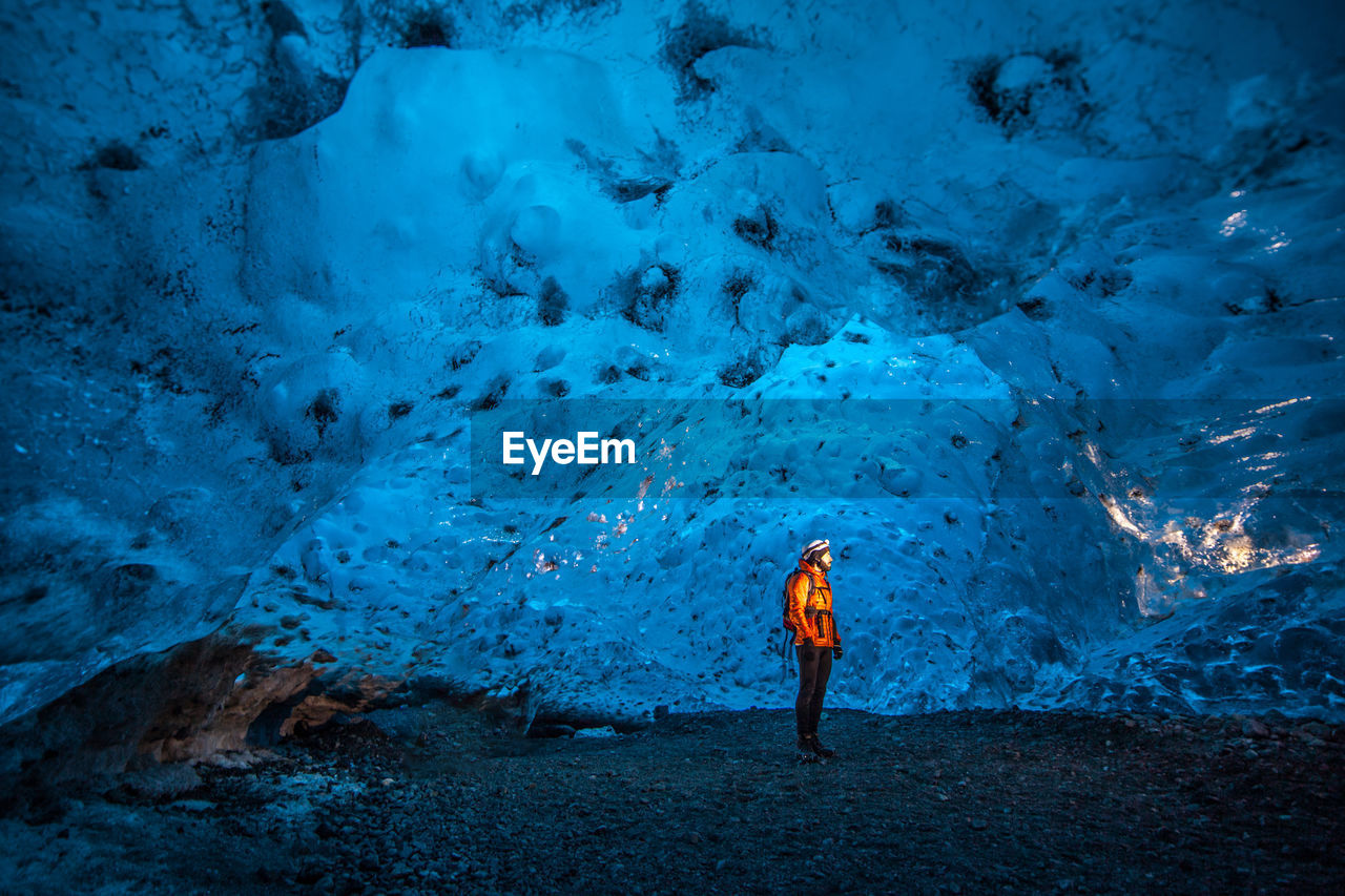 Side view of explorer standing in blue ice cave in winter during adventure in iceland