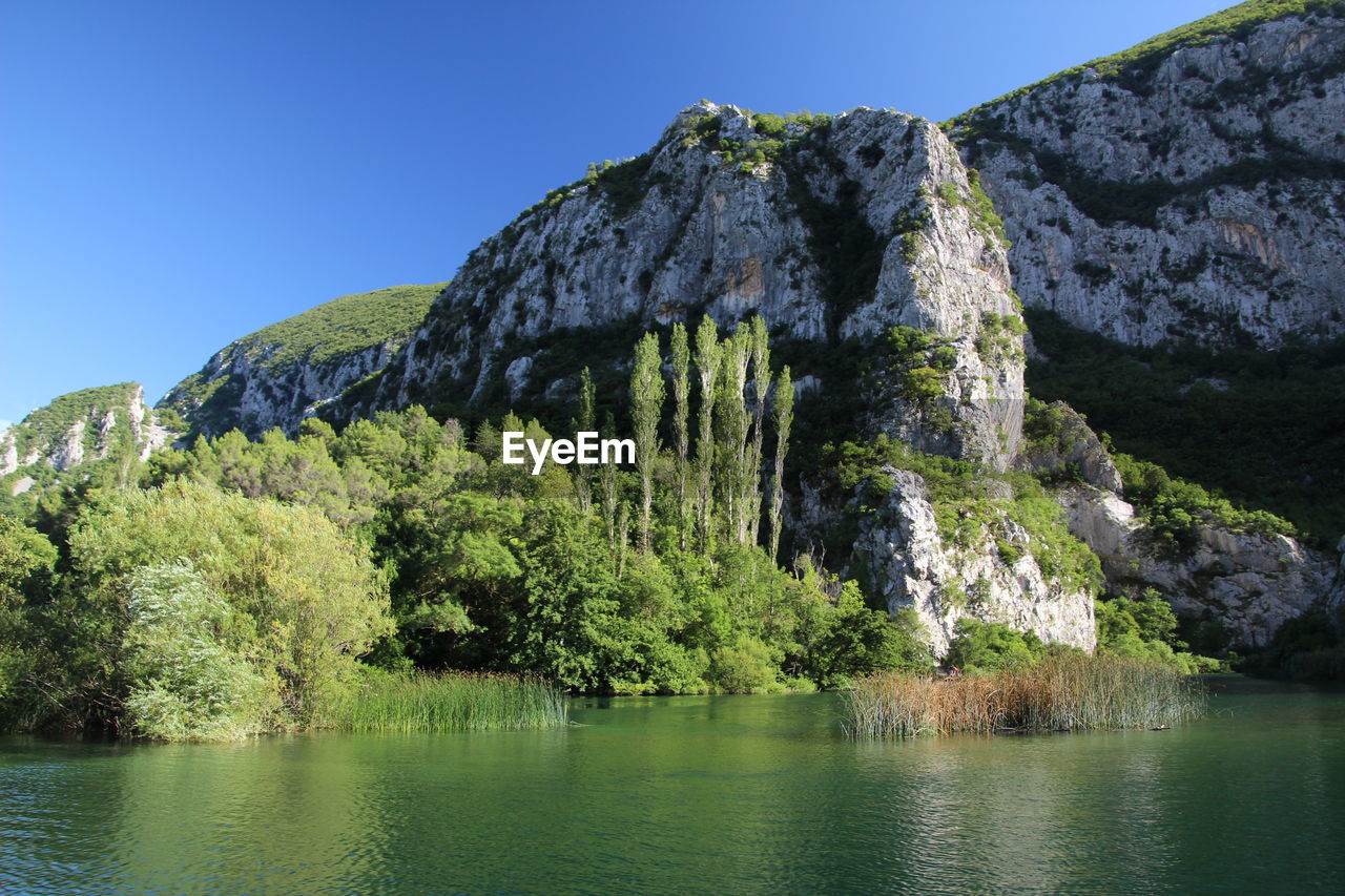 Scenic view of river by mountains against clear sky