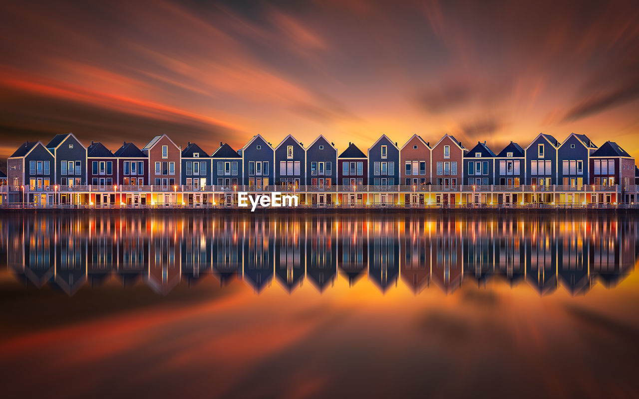Reflection of building on sea against cloudy sky during sunset