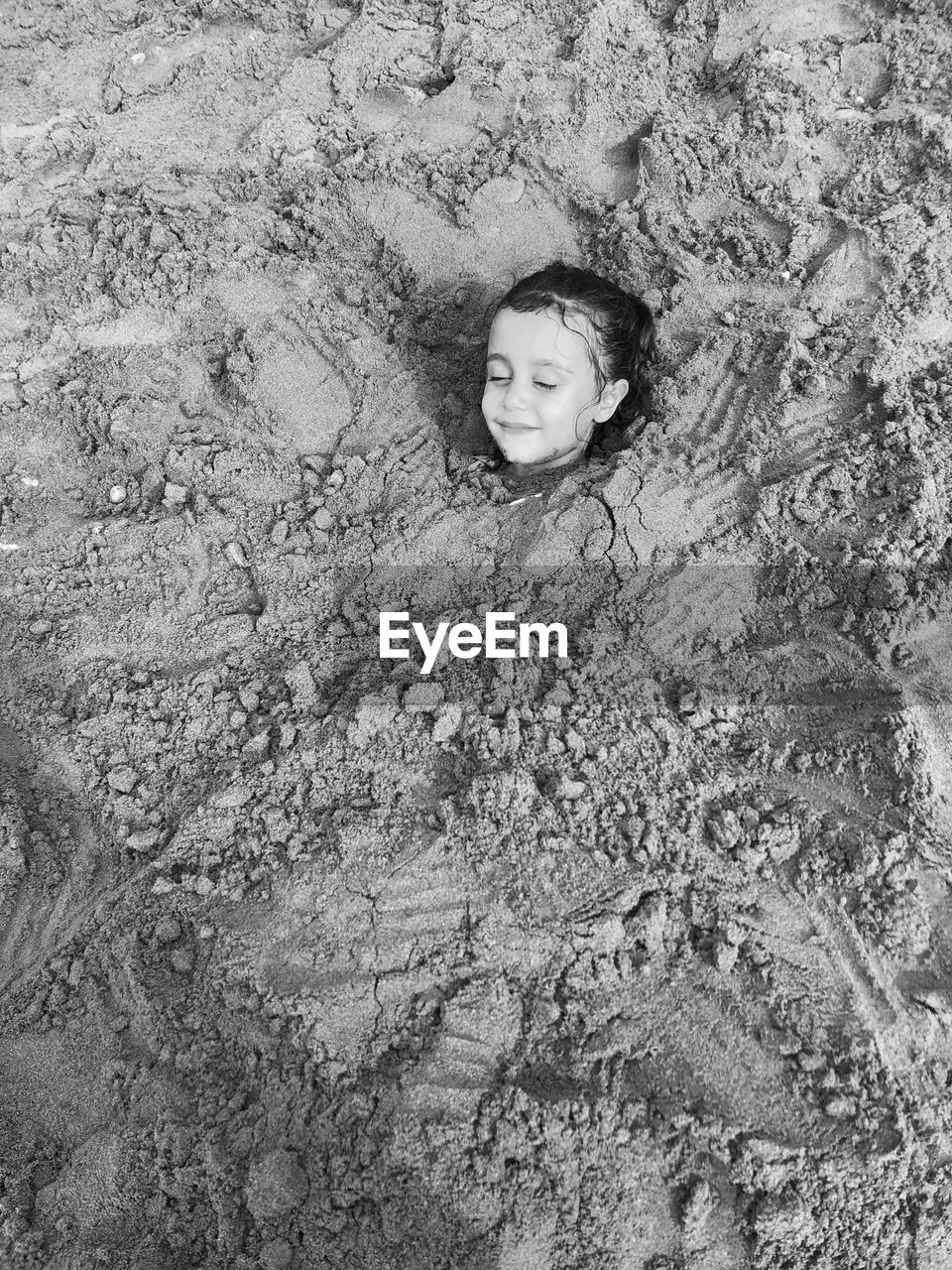 High angle view of smiling girl buried in sand