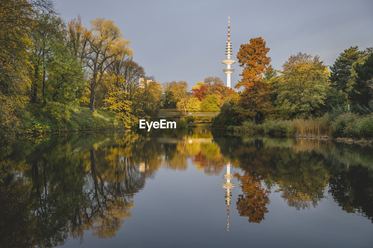 Germany, hamburg, autumn trees reflecting on surface of shiny lake in wallanlagen park