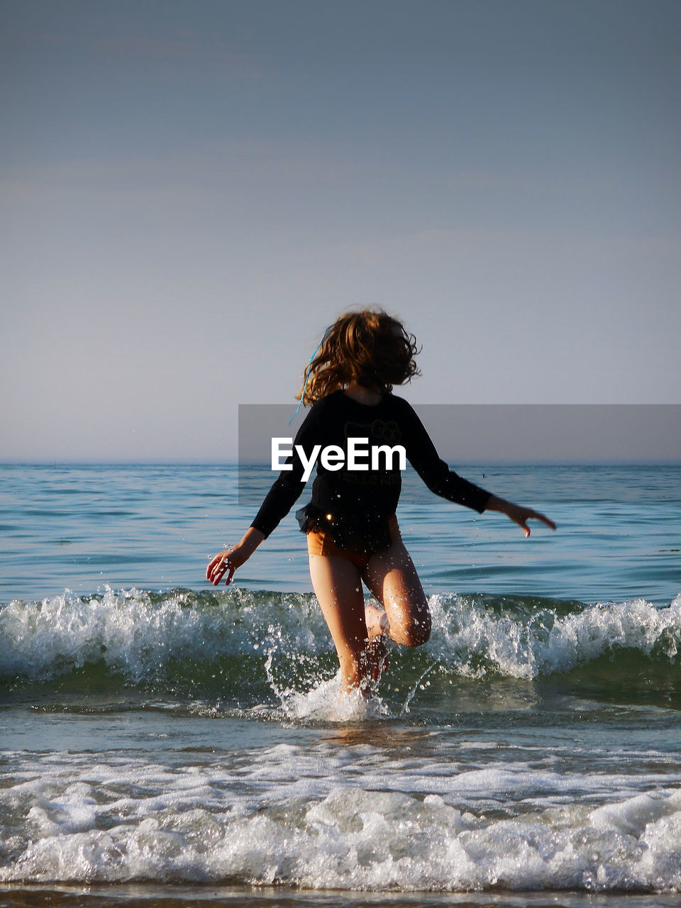 REAR VIEW OF WOMAN ON BEACH AGAINST SEA