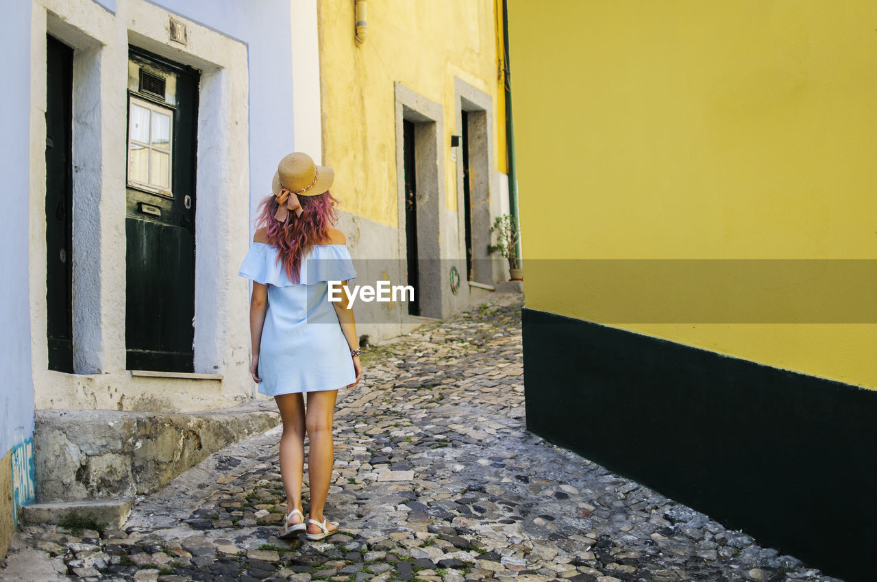 Rear view of young woman walking at alley amidst buildings