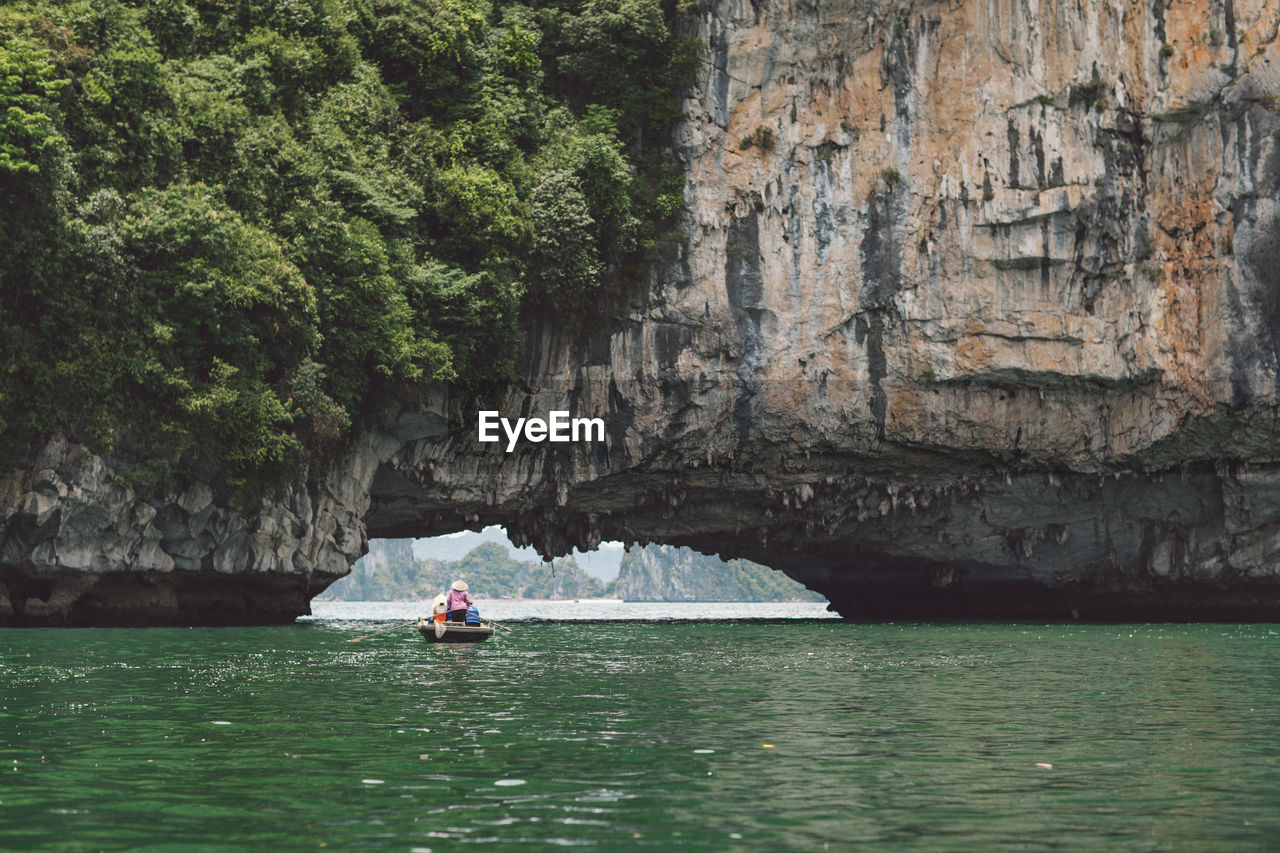 People rowing boat on halong bay under rock formation