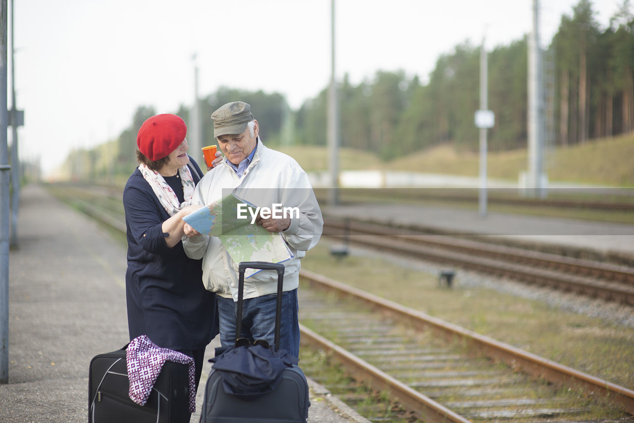 Happy senior couple with suitcases looking at the map and waiting for the train to go on a trip