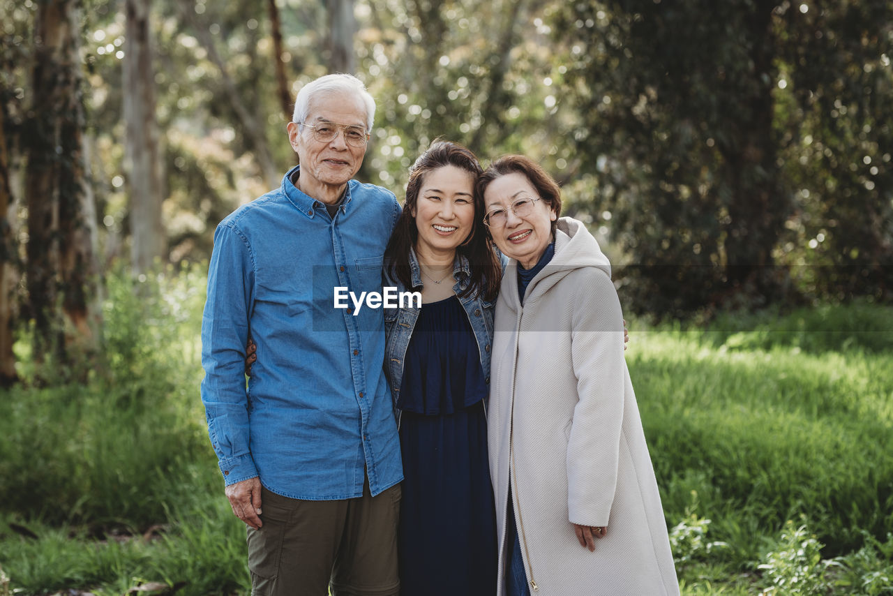 Portrait of senior active couple hugging adult daughter outside