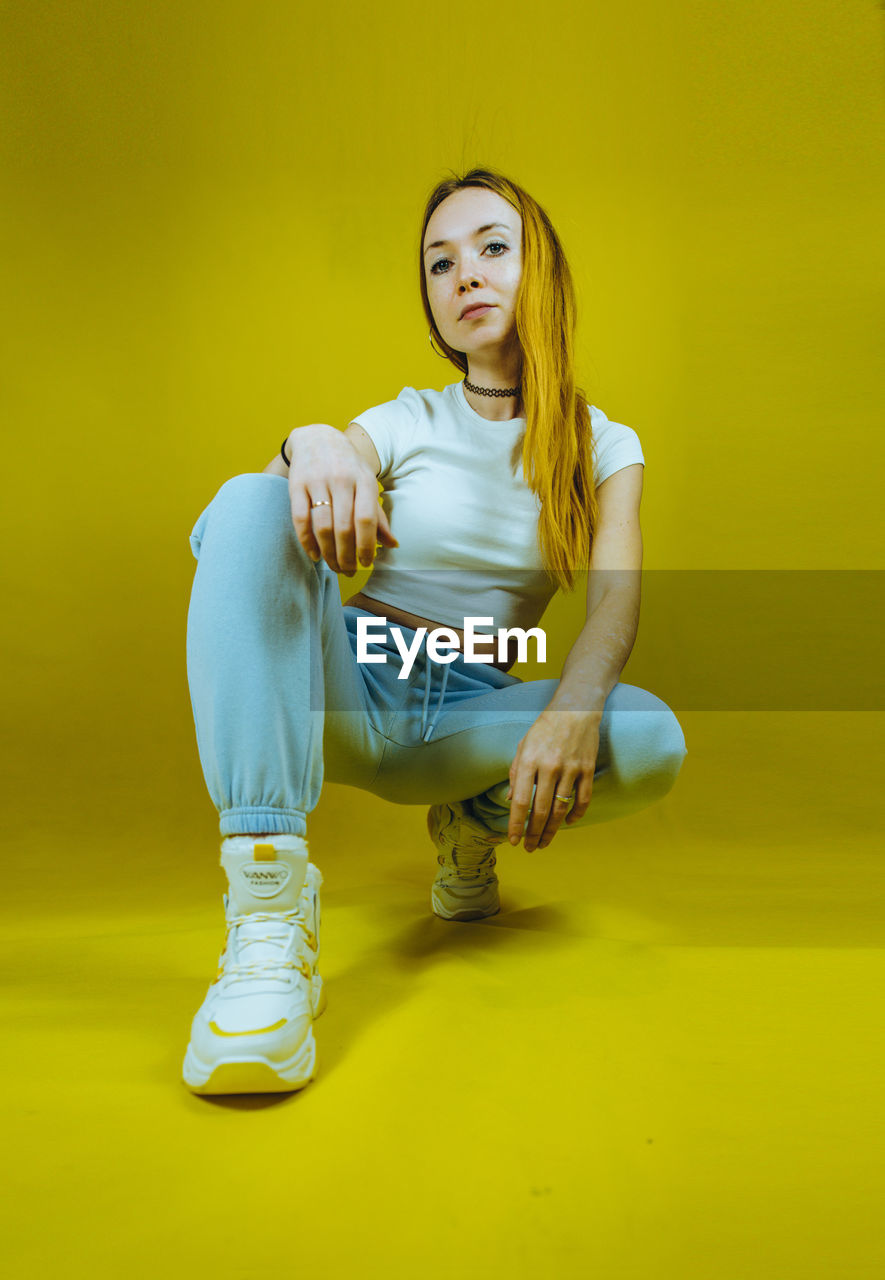 Portrait of young woman sitting against yellow background