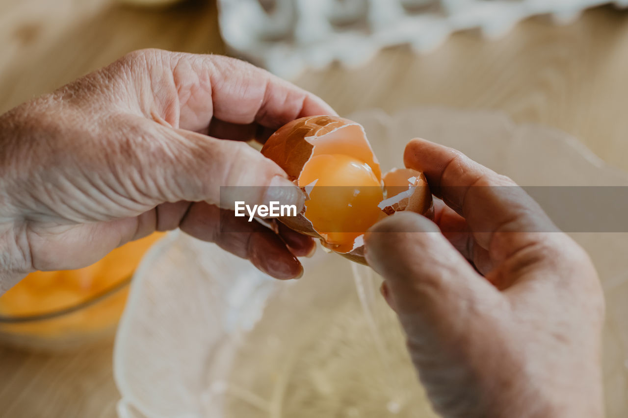 Older woman's hands with eggs preparing cakes and sweets