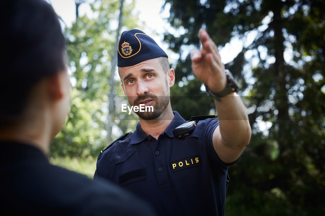 Male police officer gesturing while directing woman outdoors