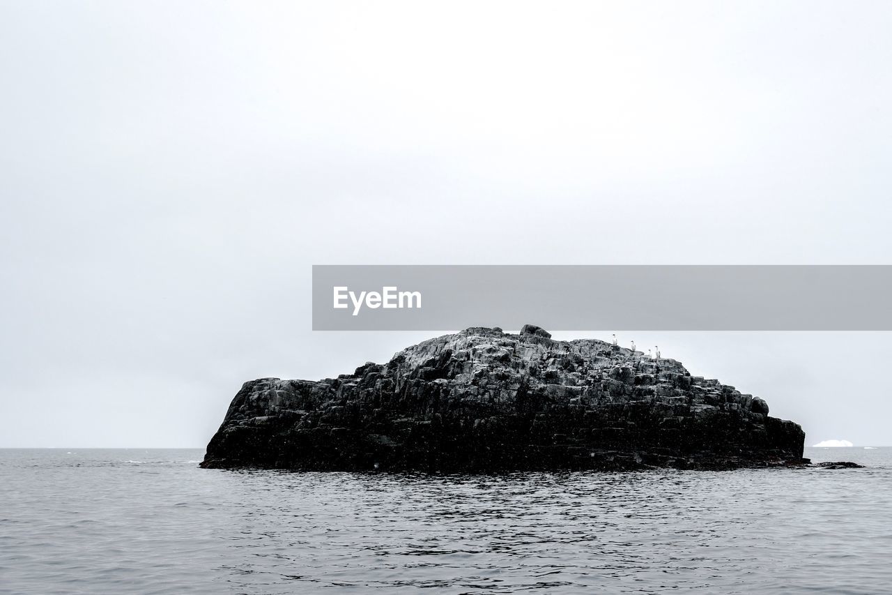 Rock formation in sea against clear sky