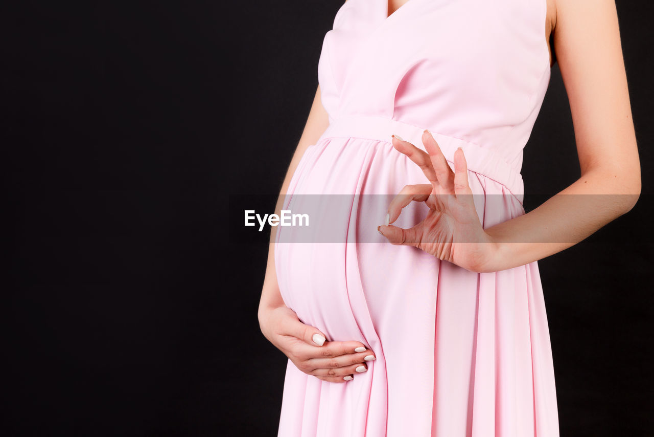 MIDSECTION OF WOMAN STANDING AGAINST PINK GRAY BACKGROUND