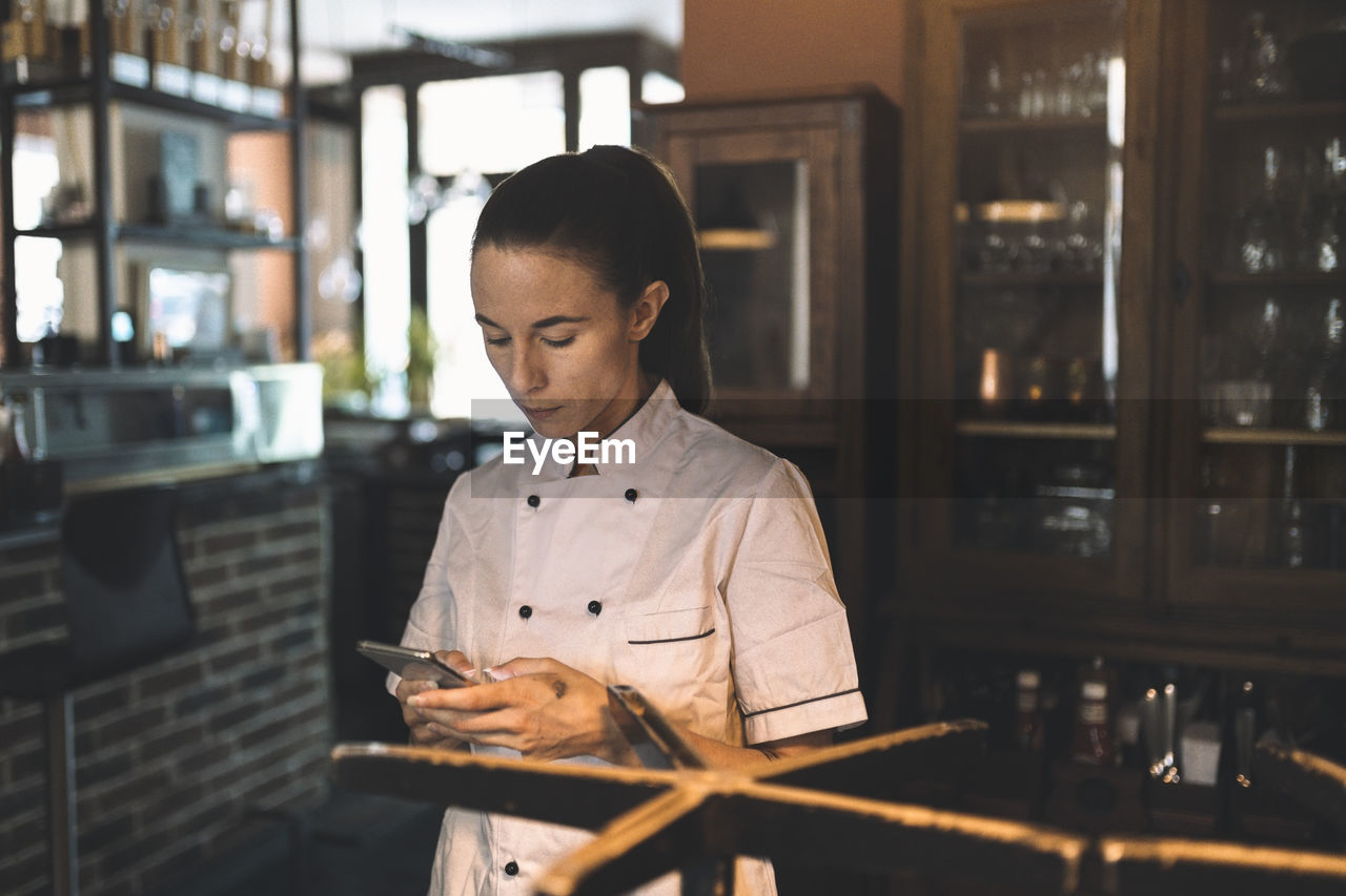 Female chef using smart phone in restaurant