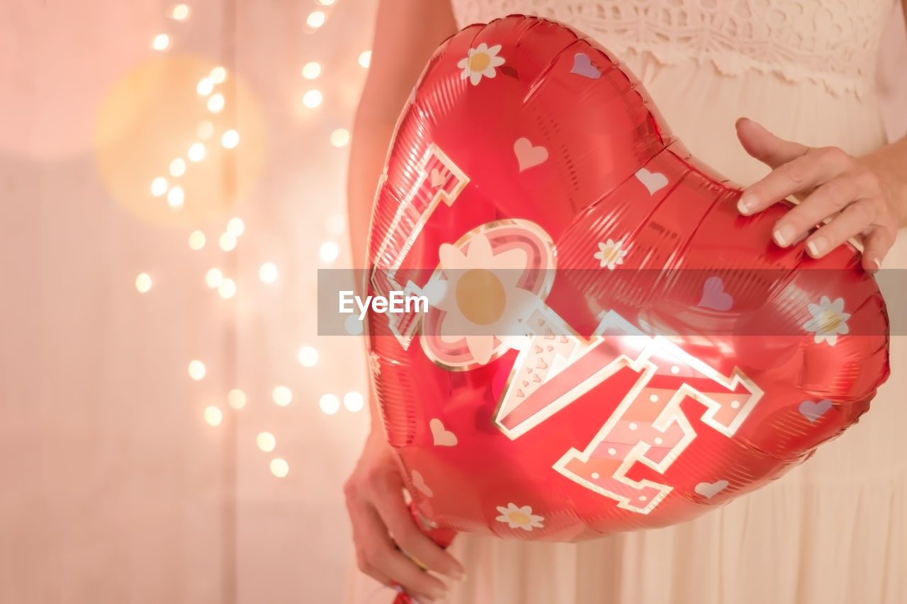 Midsection of bride holding heart shape balloon with love text against illuminated lights