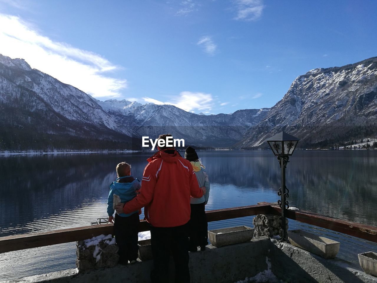 Rear view of father with children looking at lake and mountains against sky