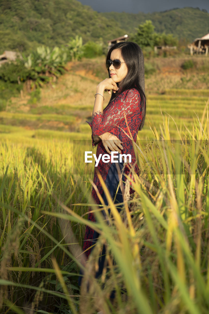 YOUNG WOMAN STANDING ON FIELD IN SUNLIGHT