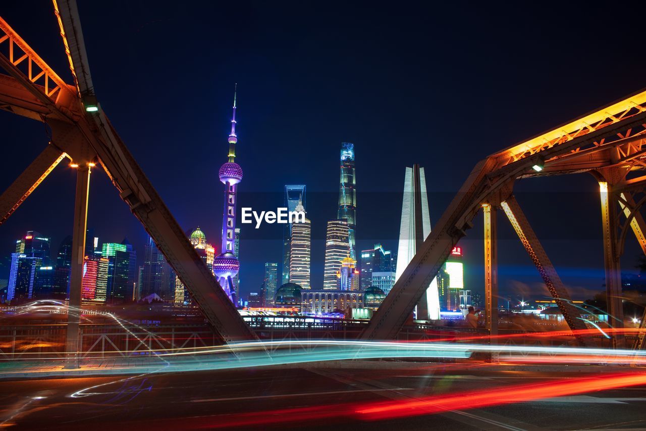 Illuminated bridge and buildings against sky at night
