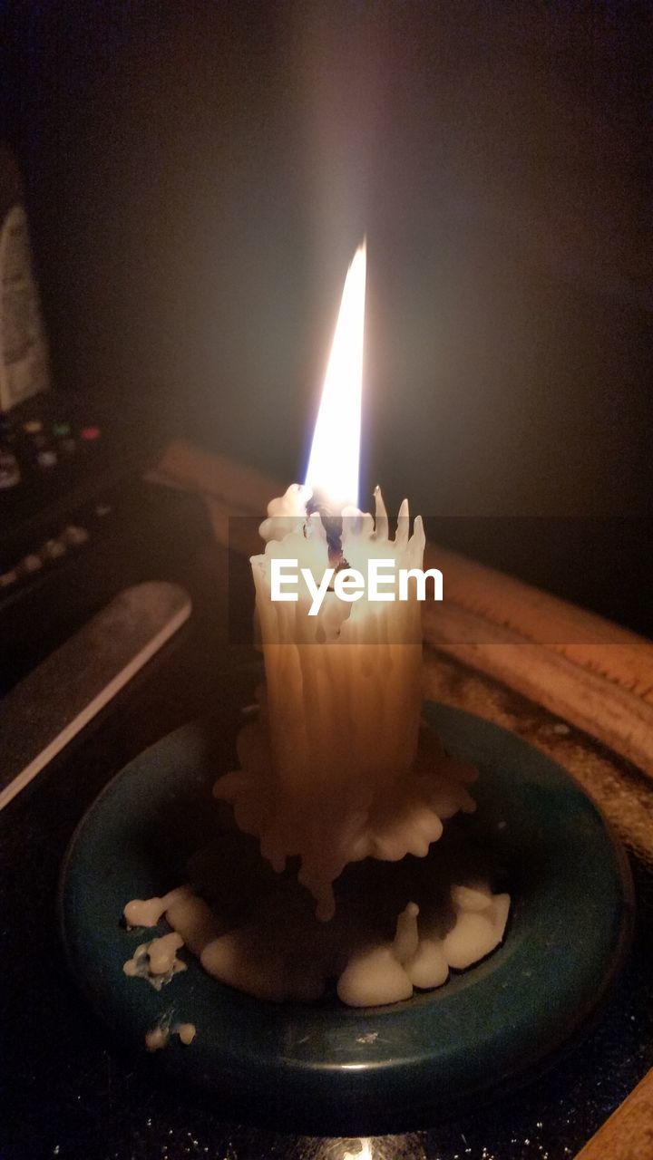 CLOSE-UP OF LIT CANDLE IN DARK ROOM