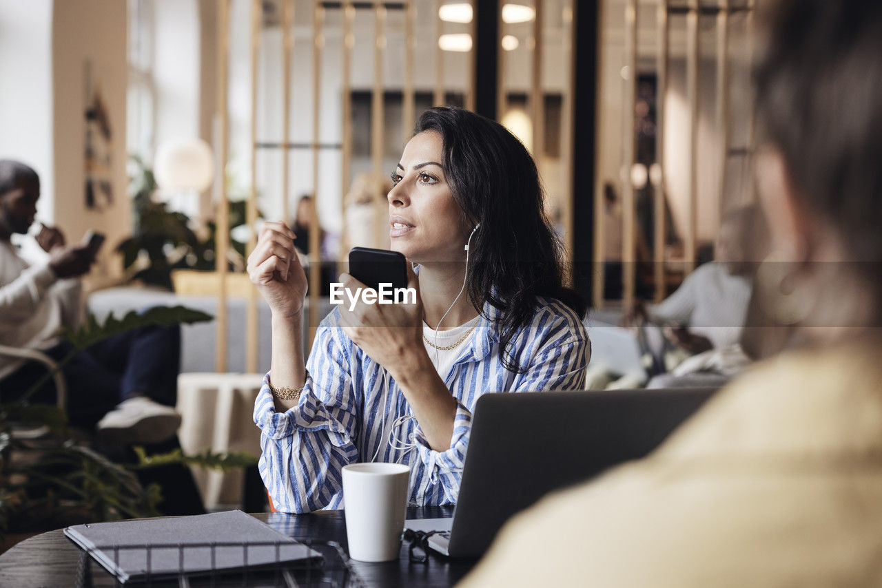 Businesswoman talking on smart phone while sitting at coworking office