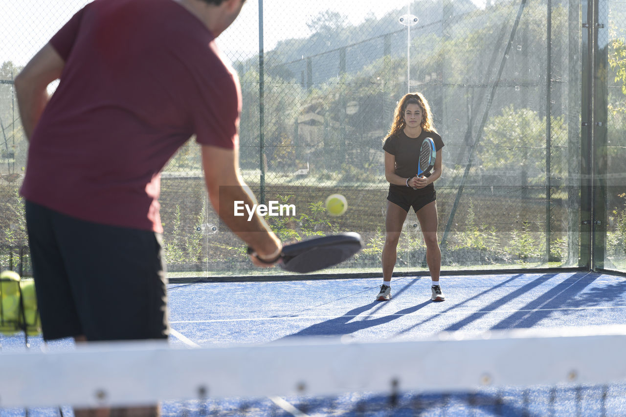 Young man playing paddle tennis with woman on sunny day