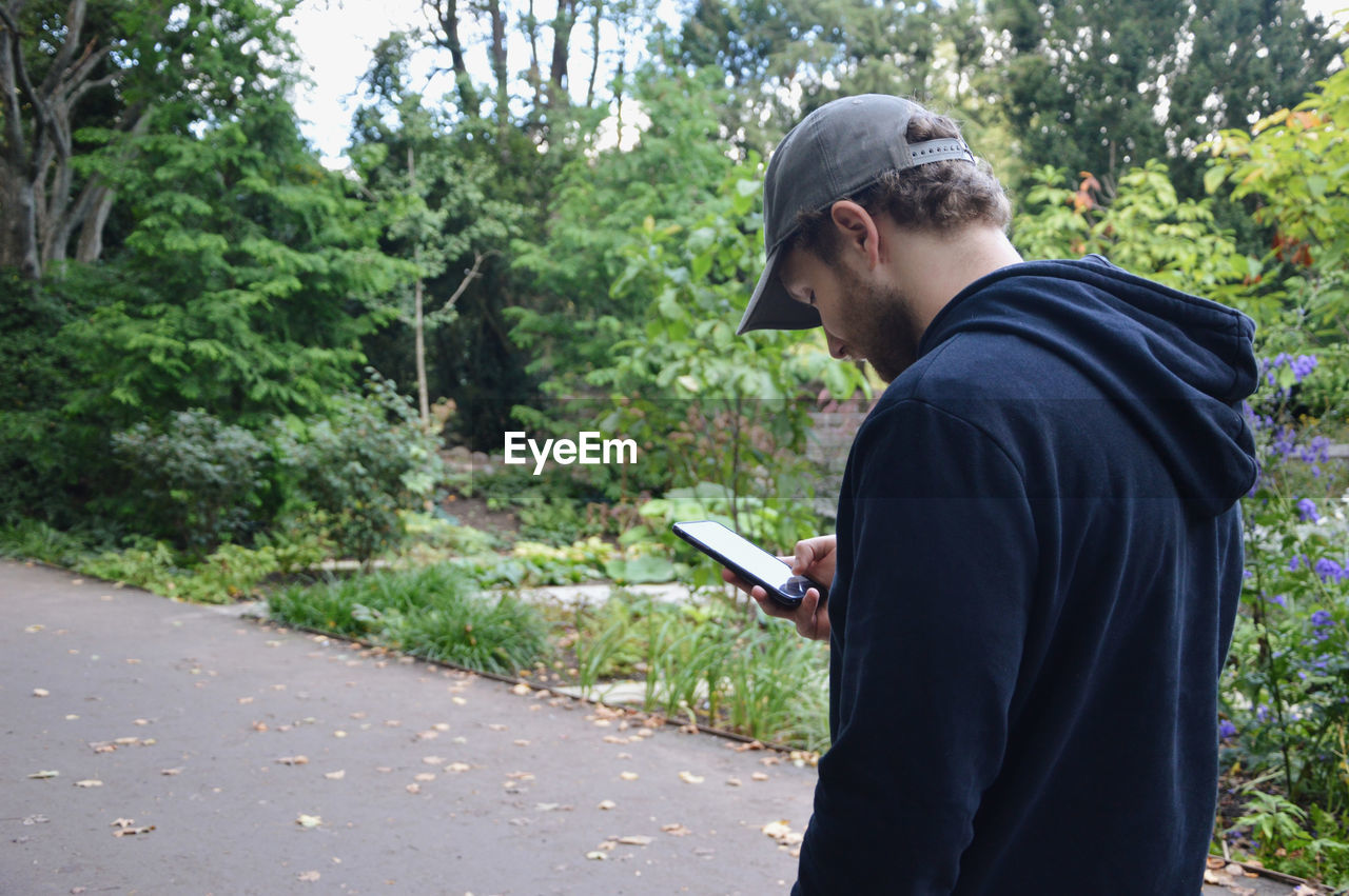 Man standing by trees and plants in park while being on his mobile phone texting