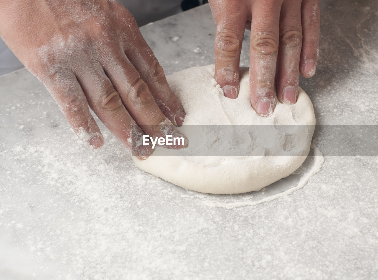 Cropped hands of chef kneading dough on table in commercial kitchen