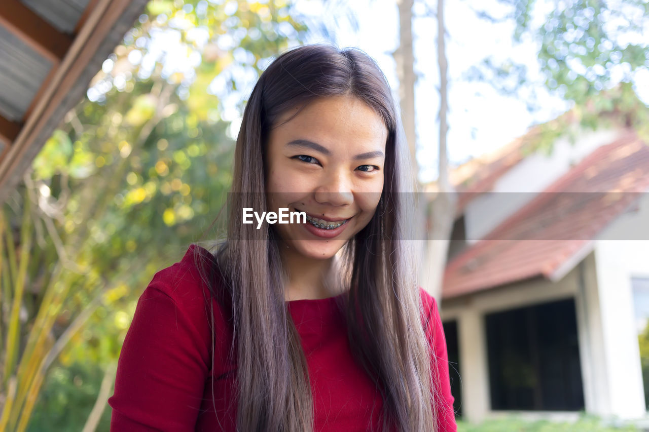 PORTRAIT OF A SMILING YOUNG WOMAN AGAINST BLURRED BACKGROUND