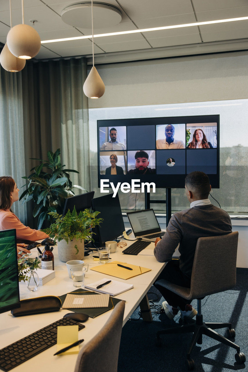 Male and female colleagues looking at tv screen during video conference in coworking office