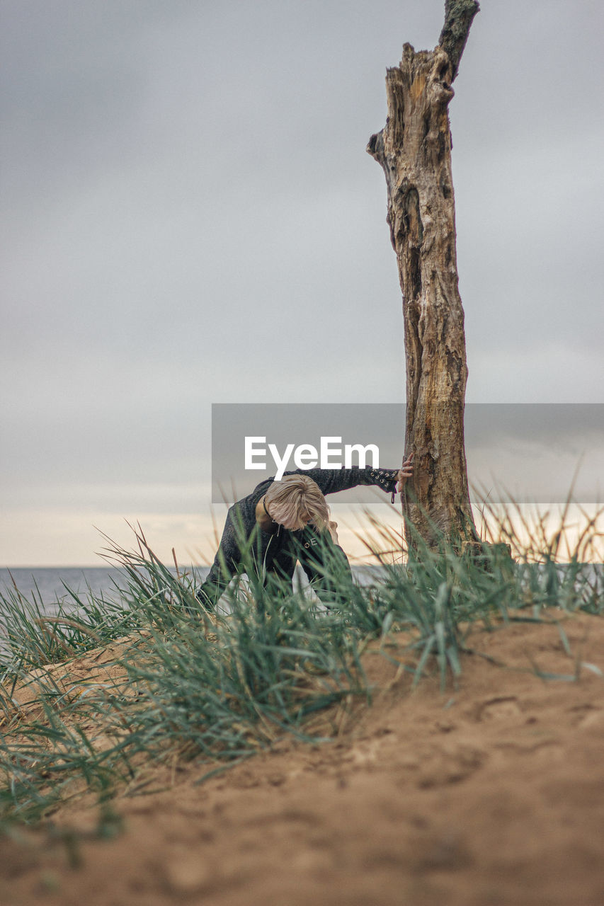 Young woman exercising while crouching by tree trunk at beach