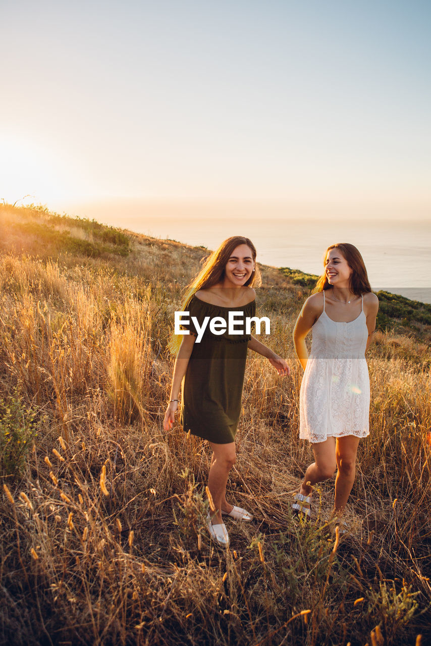 Female friends walking on land against sky during sunset