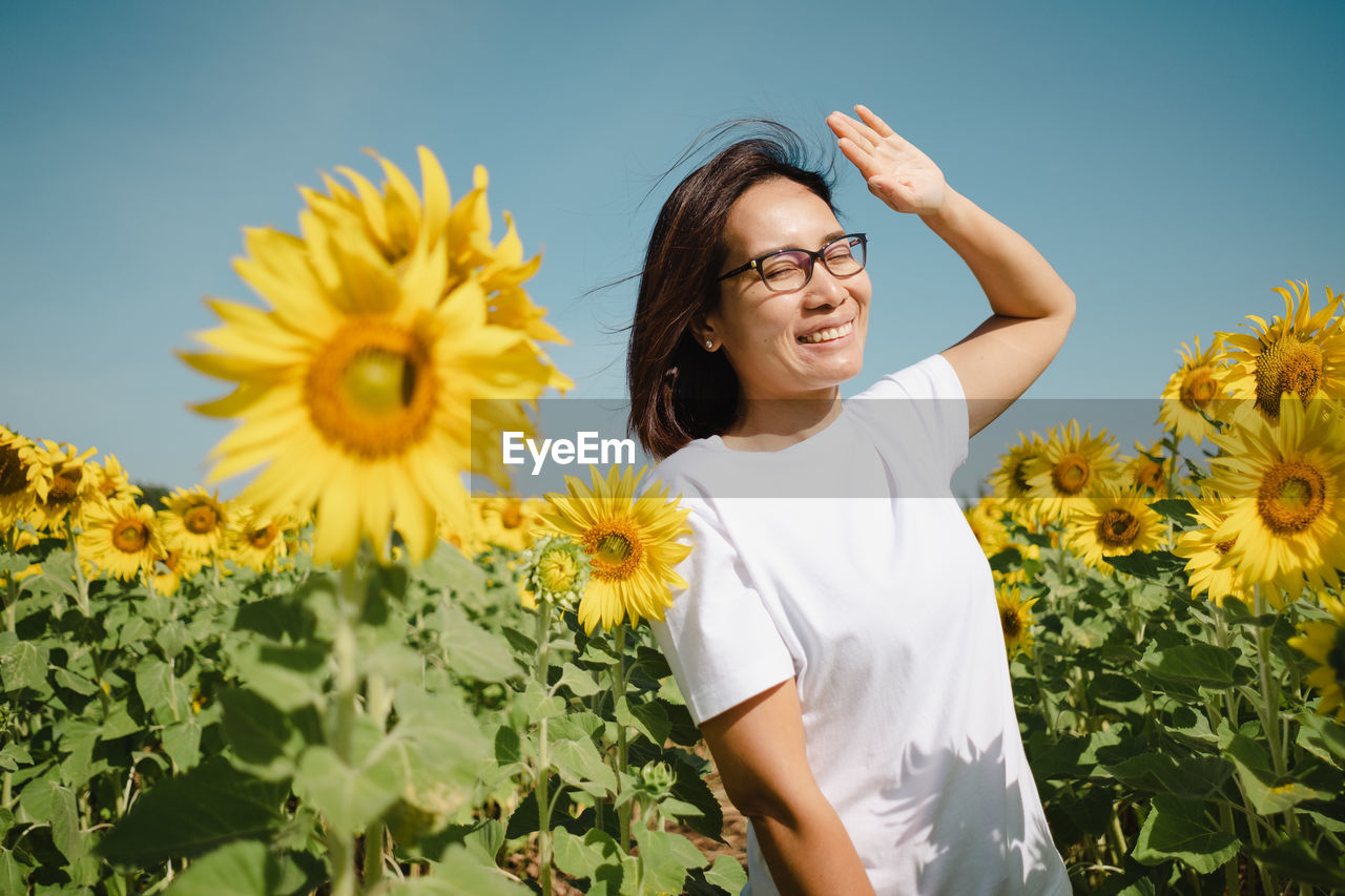 portrait of young woman with arms raised standing amidst sunflowers