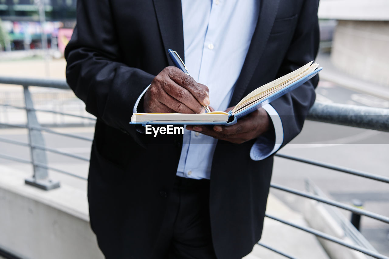 Businessman writing in diary while leaning on railing