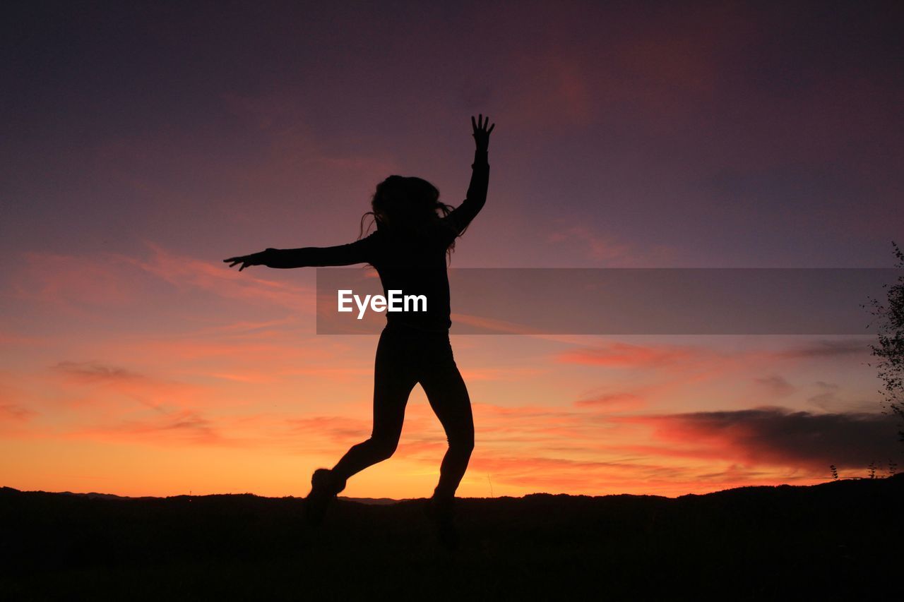 Silhouette woman with arms outstretched standing against sky during sunset