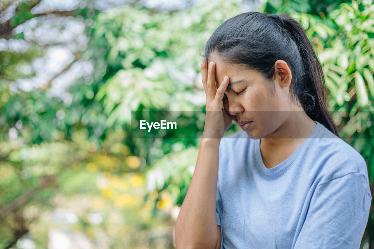 Woman touching head in pain against trees