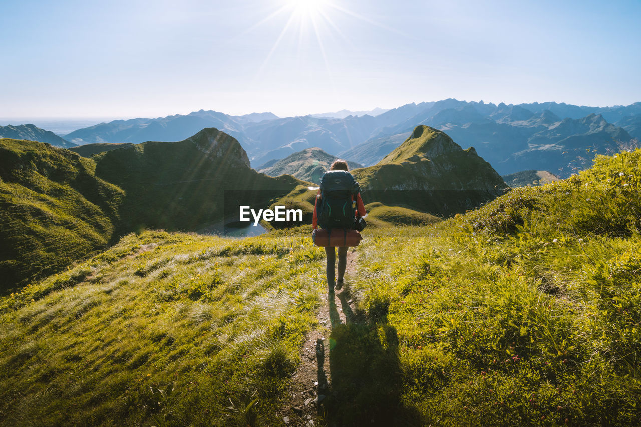 REAR VIEW OF MAN LOOKING AT MOUNTAINS AGAINST SKY