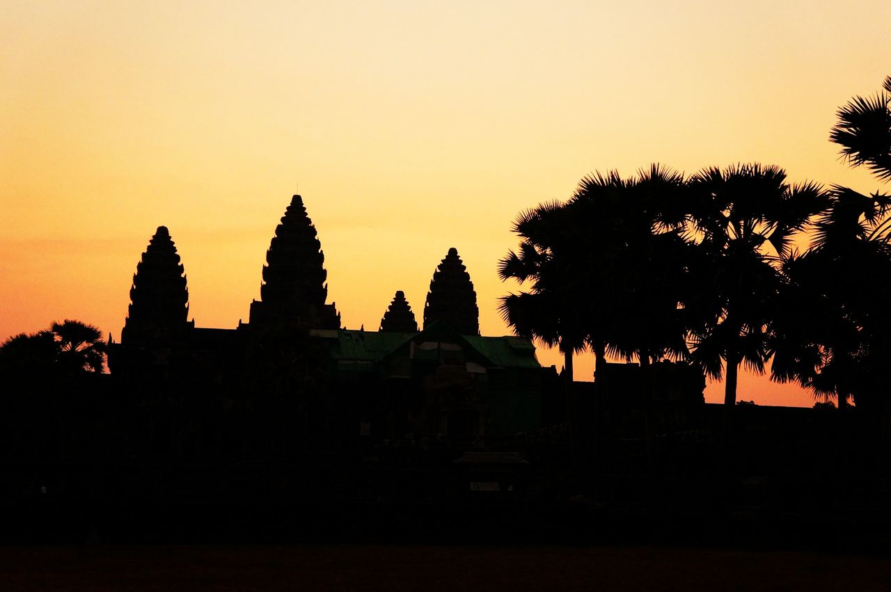 Silhouette temple and coconut palm tree against sky at sunset