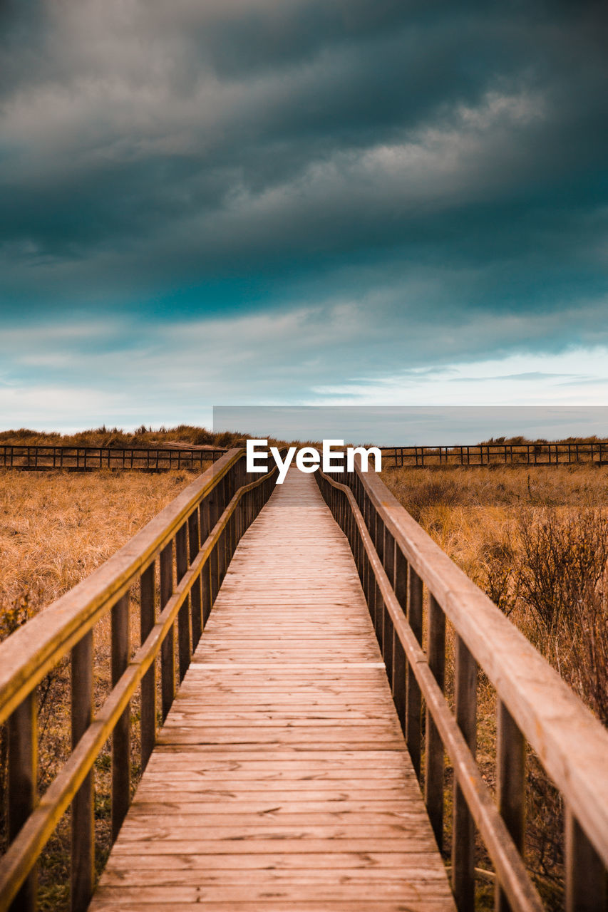 Boardwalk on field against sky