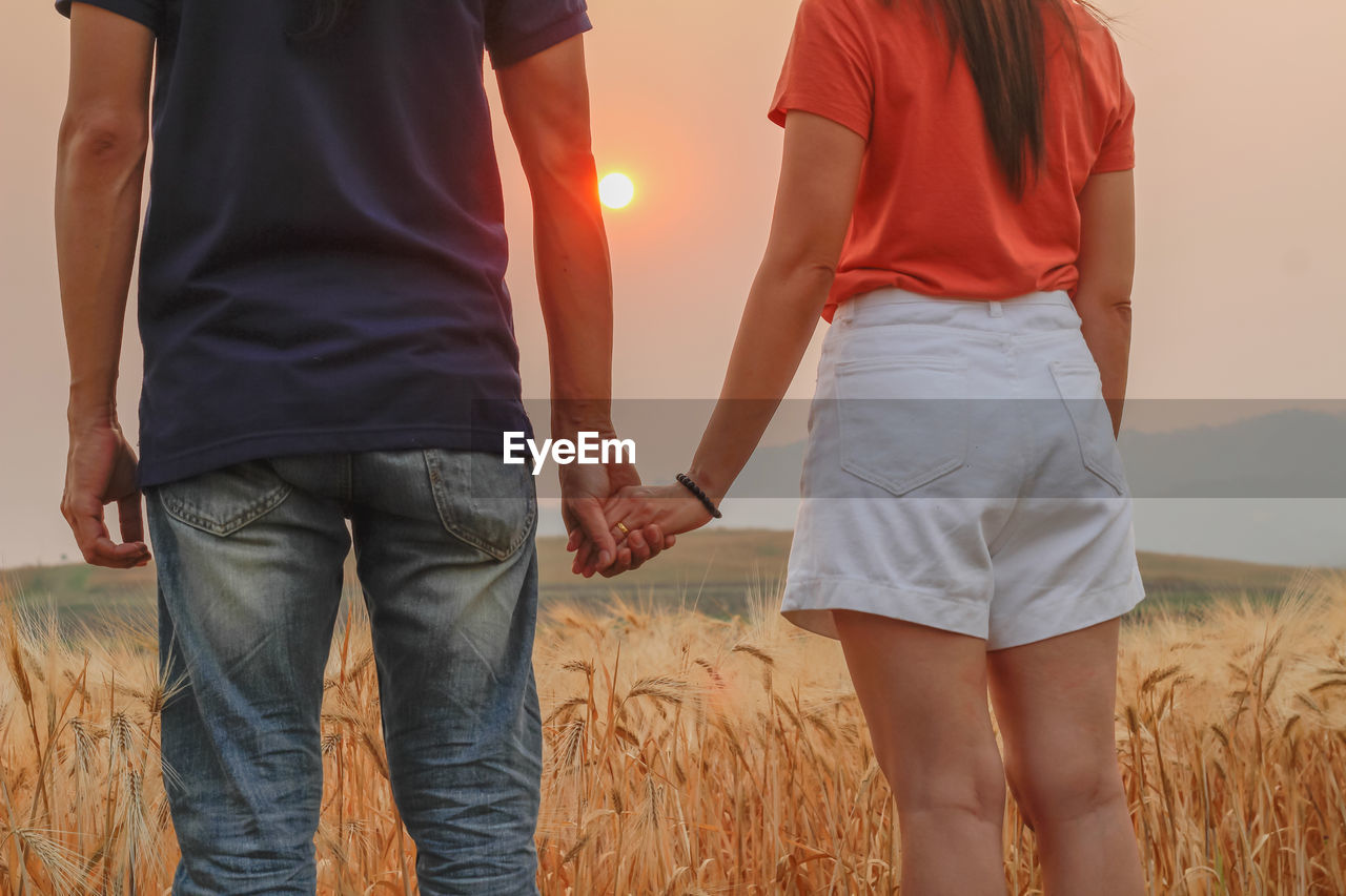 Midsection of couple standing on land during sunset