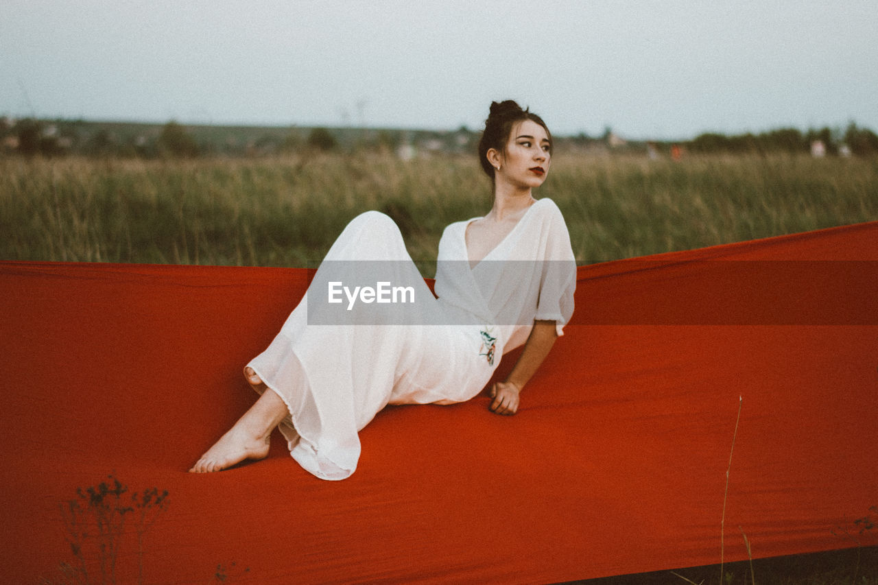 Thoughtful young woman sitting on hammock against sky