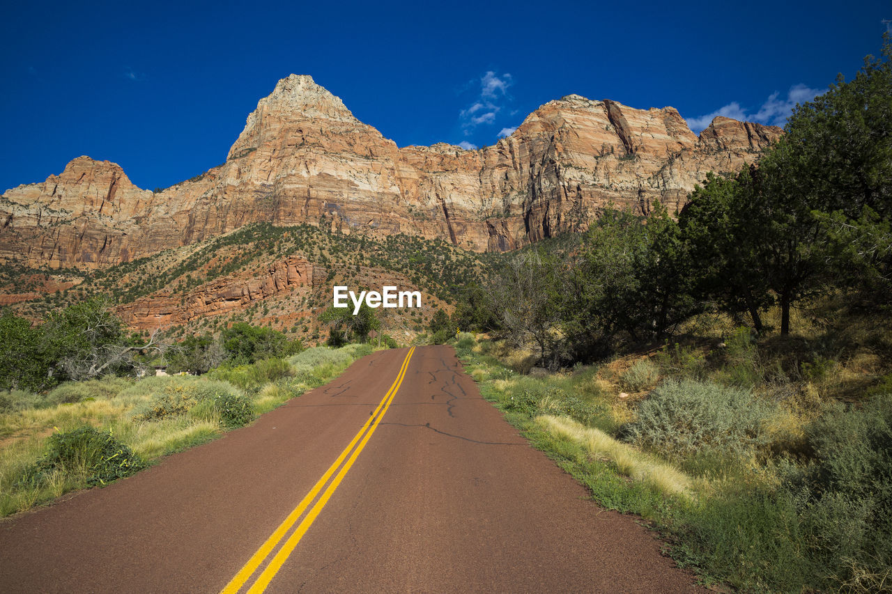 Road leading towards mountains against clear sky