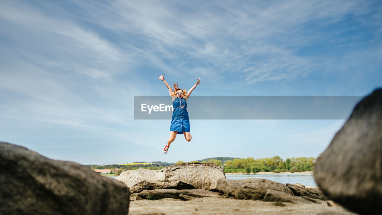 REAR VIEW OF PERSON JUMPING ON ROCK