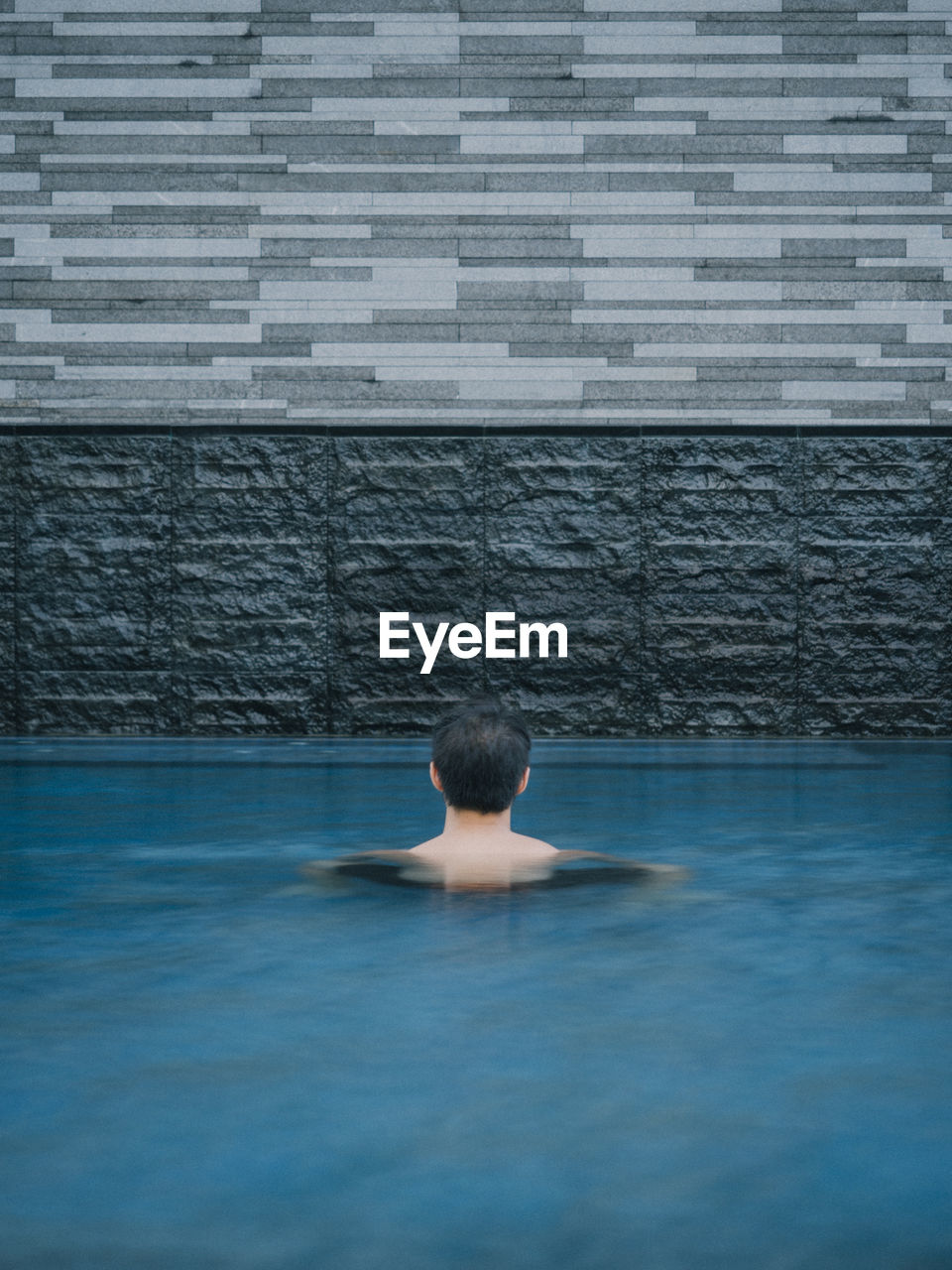 Back of asian male head in pool looking at layers