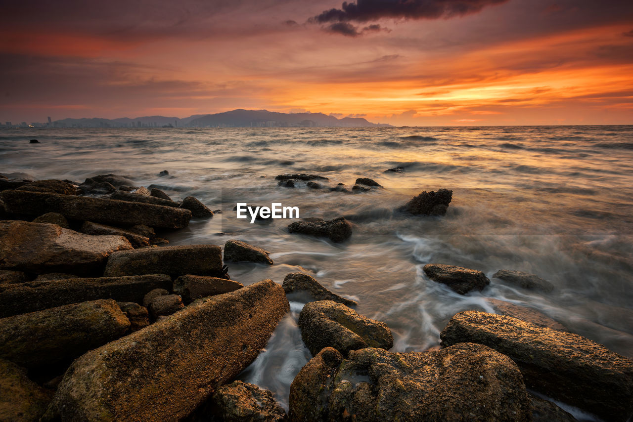 sea, water, sky, land, sunset, rock, beauty in nature, beach, scenics - nature, cloud, ocean, nature, coast, wave, shore, dawn, horizon, environment, motion, evening, wind wave, seascape, horizon over water, body of water, landscape, travel destinations, dramatic sky, sun, no people, tranquility, coastline, outdoors, travel, long exposure, sunlight, tranquil scene, idyllic, sports, sand, orange color, urban skyline, water sports