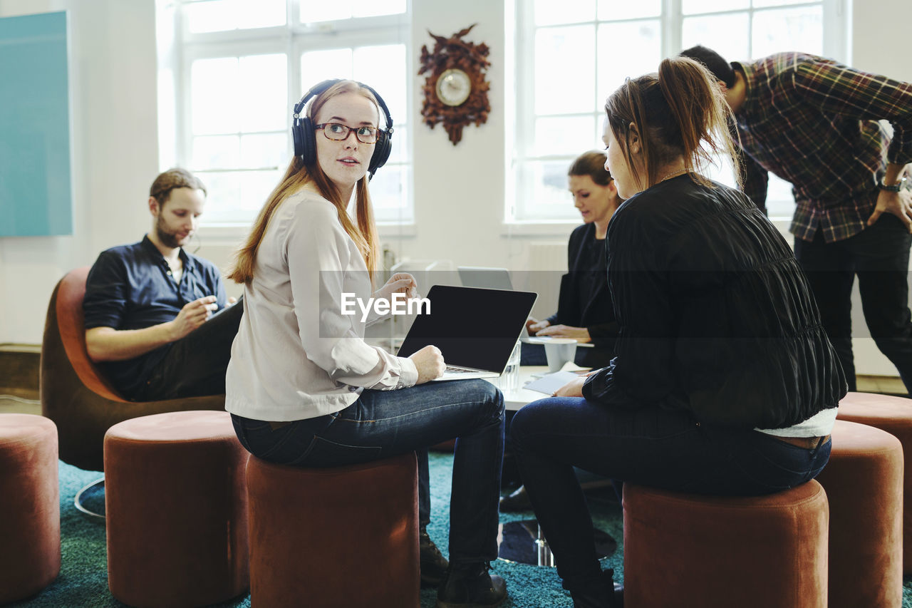 Businesswoman looking away while sitting with colleagues in creative office