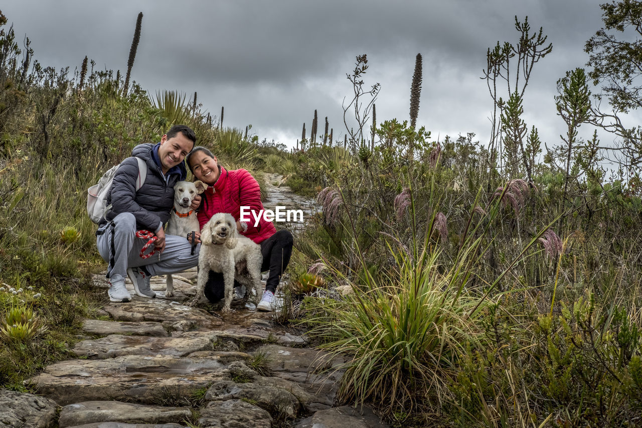 Young couple smiling with dogs on high mountain stone path front view